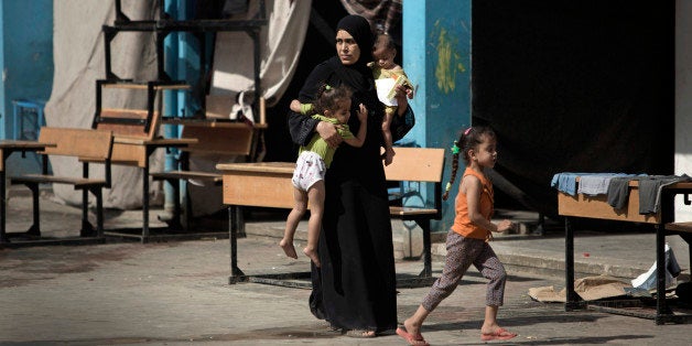 In this Wednesday, Sept. 3, 2014 photo, a Palestinian woman carries two children as she walks in a U.N. school where she lives with her family after her house was destroyed by Israeli strikes in Gaza City. Israeli airstrikes have left much of the territory in ruins, and thousands of homes have been destroyed or severely damaged. Reconstruction has yet to begin as a blockade imposed by Egypt and Israel on Gaza still holds, severely restricting the import of cement and other building materials. (AP Photo/Khalil Hamra)