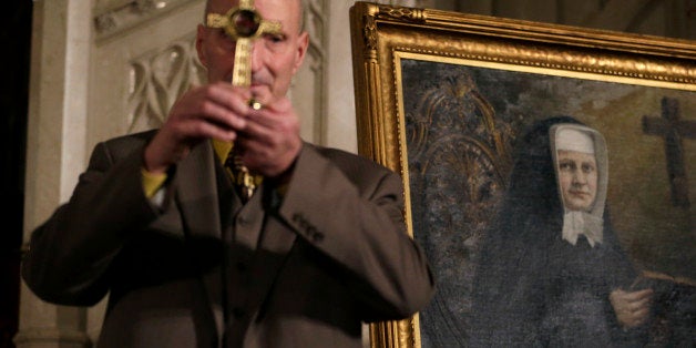 A painting of Sister Miriam Teresa Demjanovich is displayed while Michael Mencer holds a cross with a lock of hair of the nun during a beatification ceremony at Cathedral Basilica of the Sacred Heart, Saturday, Oct. 4, 2014, in Newark, N.J. Demjanovich, who died in 1927 at age 26, is credited with curing Mencer's eye disease as a boy when he was given a lock of the nun's hair and prayed to her. The ceremony moves Demjanovich a step closer to sainthood with her beatification as it is the third in a four-step process. (AP Photo/Julio Cortez)