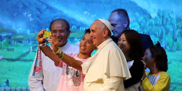 Pope Francis poses for a selfie with young people during a meeting with Asian youth at the Solmoe Sanctuary in Dangjin, South Korea, Friday, Aug. 15, 2014. Pope Francis urged Catholic youth on Friday to renounce the materialism that afflicts much of Asian society today and reject "inhuman" economic systems that disenfranchise the poor, pressing his economic agenda in one of the region's powerhouses where financial gain is a key barometer of success. (AP Photo/Ahn Young-joon, Pool)