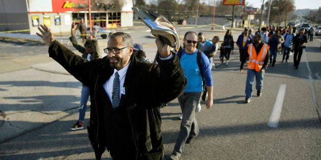 A large group walks past a burned-out business Saturday, Nov. 29, 2014, in Ferguson, Mo., early in a 120-mile march to the governor's mansion in Jefferson City. The march, organized by the NAACP to evoke civil rights marches from the 1960s, began Saturday afternoon on Canfield Drive in Ferguson where Michael Brown was killed and is expected to last seven days. (AP Photo/Jeff Roberson)