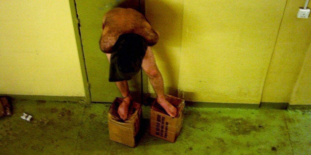 This is an image obtained by The Associated Press which shows a detainee standing on MRE boxes with a hood over his head in l