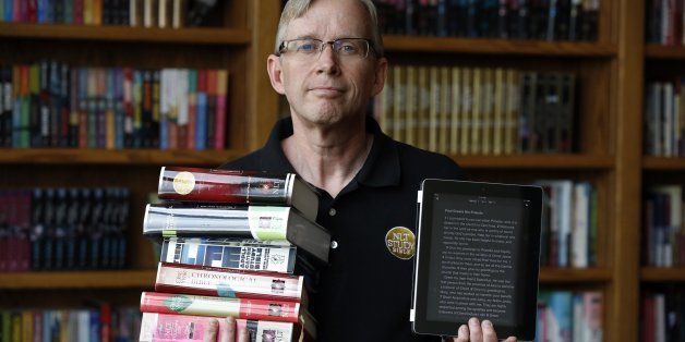 Jeffrey Smith, New Living Translation brand director at Tyndale House Publishers, poses with a stack of some of the different editions of the New Living Bible used in the free You Version app, opened on his iPad, August 15, 2013 in Carol Stream, Illinois. (Chuck Berman/Chicago Tribune/MCT via Getty Images)