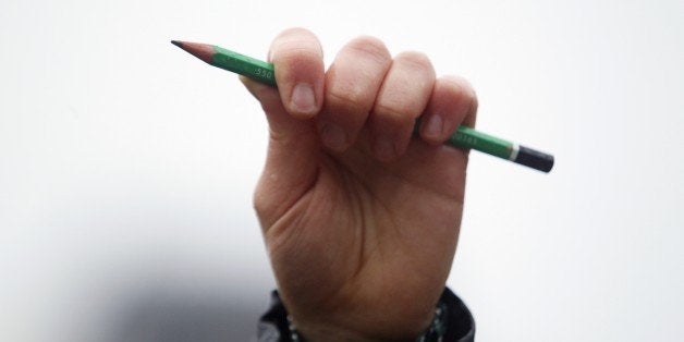 A man holds a pencil in the air as he stands in front of Notre-Dame de Paris Cathedral in Paris to observe a minute of silenc