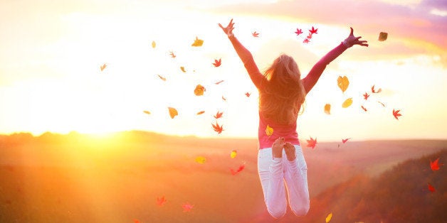 Woman jumping in the countryside at sunset with autumn leaves in the air.