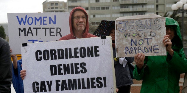 Billy Bradford, left, and others hold up signs as they gather with students and supporters at a vigil outside of St. Mary's Cathedral in San Francisco, Friday, Feb. 6, 2015. The Roman Catholic archbishop of San Francisco is getting pushback from some parents, students and teachers at parochial schools after unveiling faculty handbook language calling on teachers to lead their public and professional lives consistently with church teachings on homosexuality, same-sex marriage, abortion, birth control and other behaviors he describes as evil. (AP Photo/Jeff Chiu)