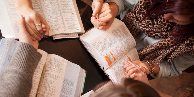 A group of young women bow their heads and pray with bibles.