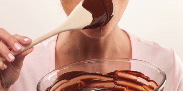 Woman with pink lipstick licking chocolate batter from wooden spoon