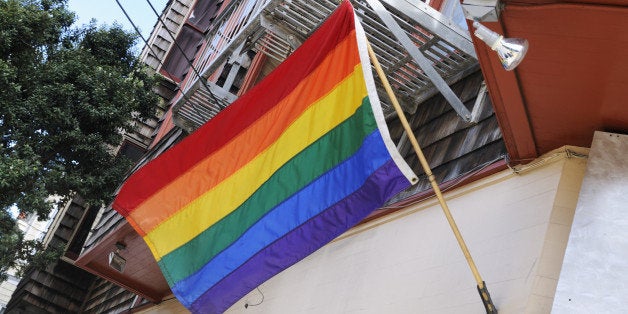 'This is a horizontal, color photograph of a Rainbow Flag in San Francisco's Castro neighborhood. There is slight motion blur