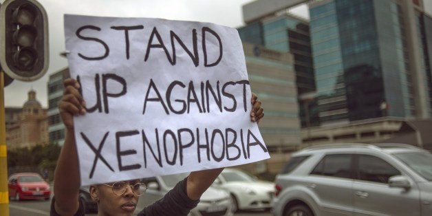 A South African holds a sign as she stands on the side od a road in Sandton, as xenophobic violence continued, on April 18, 2