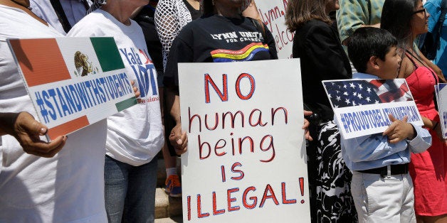 Lucy Francis, of Lynn, Mass., center, displays a placard and chants slogans during a rally, Tuesday, July 22, 2014, on the steps of City Hall, in Lynn, Mass., held to protest what organizers describe as the scapegoating of immigrants for problems in the city. The mayor of Lynn and education officials complain their schools are being overwhelmed by young Guatemalans who speak neither English or Spanish as their first language. (AP Photo)