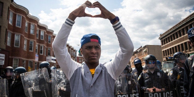 BALTIMORE, MD - APRIL 28: A man makes a heart shape with his hands during a protest near the CVS pharmacy that was set on fire yesterday during rioting after the funeral of Freddie Gray, on April 28, 2015 in Baltimore, Maryland. Gray, 25, was arrested for possessing a switch blade knife April 12 outside the Gilmor Houses housing project on Baltimore's west side. According to his attorney, Gray died a week later in the hospital from a severe spinal cord injury he received while in police custody. (Photo by Andrew Burton/Getty Images)