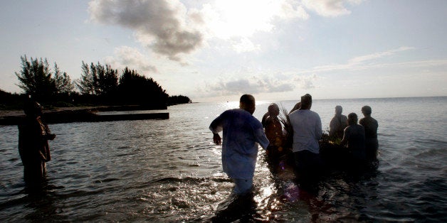 A group of men wade into the ocean as they push a small raft loaded with offerings to their ancestors out to sea Sunday, June