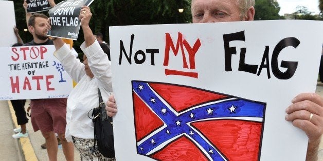 A man holds a sign up during a protest rally against the Confederate flag in Columbia, South Carolina on June 20, 2015. The racially divisive Confederate battle flag flew at full-mast despite others flying at half-staff in South Carolina after the killing of nine black people in an historic African-American church in Charleston on June 17. Dylann Roof, the 21-year-old white male suspected of carrying out the Emanuel African Episcopal Methodist Church bloodbath, was one of many southern Americans who identified with the 13-star saltire in red, white and blue. AFP PHOTO/MLADEN ANTONOV (Photo credit should read MLADEN ANTONOV/AFP/Getty Images)