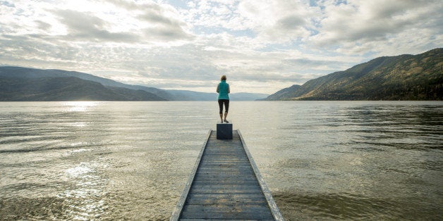 Woman stand at end of pier above lake