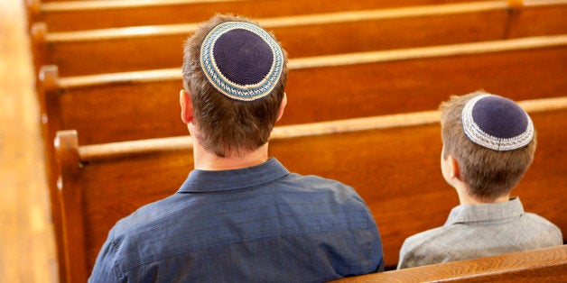 Father and son in yarmulkes sitting in synagogue