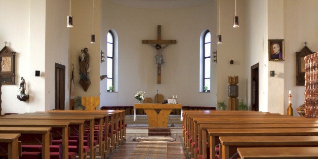 Inside of a large, traditional catholic church with pews and cross visible.