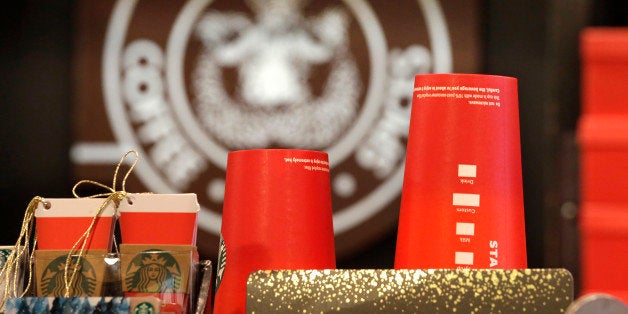 Red paper cups are stacked in view of the company logo behind the counter at a Starbucks coffee shop in the Pike Place Market, Tuesday, Nov. 10, 2015, in Seattle. It's as red as Santa's suit, a poinsettia blossom or a loud Christmas sweater. Yet Starbucks' minimalist new holiday coffee cup has set off complaints that the chain is making war on Christmas. (AP Photo/Elaine Thompson)