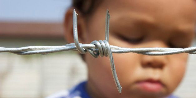 Sad Asian boy behind barbed wire. Focus on barbed wire. Like a refugee camp.