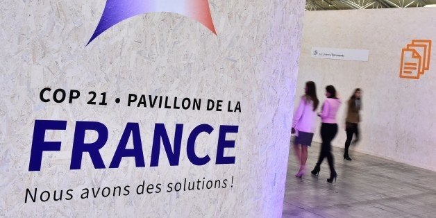 People walk by a poster hanging outside of the France pavilion reading 'We have solutions !' during the United Nations conference on climate change COP21, on December 1, 2015 at Le Bourget, on the outskirts of the French capital Paris. More than 150 world leaders are meeting under heightened security, for the 21st Session of the Conference of the Parties to the United Nations Framework Convention on Climate Change (COP21/CMP11), also known as Paris 2015 from November 30 to December 11. / AFP / LOIC VENANCE (Photo credit should read LOIC VENANCE/AFP/Getty Images)