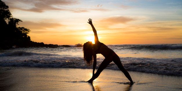 A woman doing yoga on the beach during sunset.