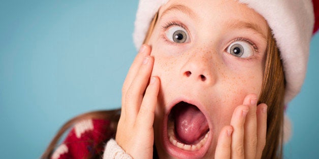 Color image of a little girl with a stressed/shocked/surprised look on her face. She is wearing a Santa hat and an ugly Chris