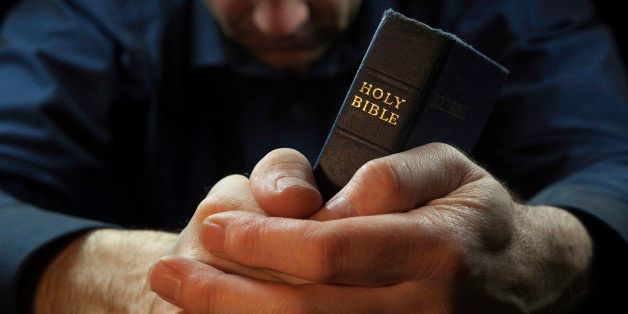 Man praying while holding a Holy Bible.