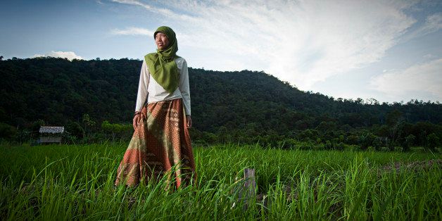 A young Indonesian woman in Muslim dress gazes out from a rice paddy near Gunung Palung National Park, Kalimantan Indonesia.