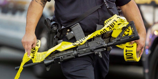 A police officer deploys tape to an area near where authorities stopped a vehicle in San Bernardino, Calif., Wednesday, Dec. 2, 2015. Multiple attackers opened fire on a banquet at a social services center for the disabled in San Bernardino on Wednesday, killing multiple people and sending police on a manhunt for suspects. (AP Photo/Damian Dovarganes)