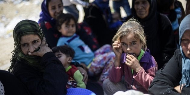 Syrian refugees sit on the side of a road that leads to the Akcakale border gate as they wait to return to their home in the