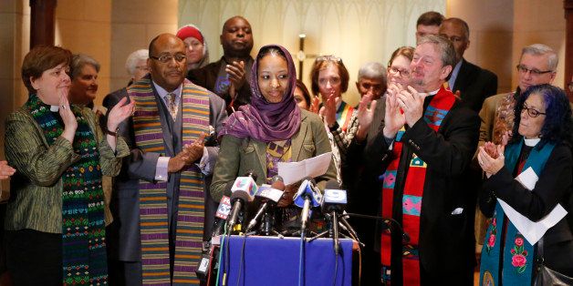 Wheaton College associate professor Larycia Hawkins, center, is greeted with applause from supporters as she begins her remarks during a news conference Wednesday, Dec. 16, 2015, in Chicago. Hawkins, a Christian teaching political science at the private evangelical school west of Chicago, who is wearing a headscarf to demonstrate solidarity with Muslims was put on leave Tuesday after making statements about the faiths' similarities that the college said conflicted with its "distinctively evangelical" identity. (AP Photo/Charles Rex Arbogast)