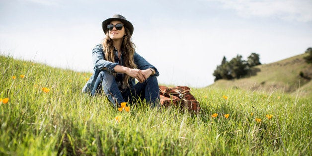 A woman with a backpack and hat sitting in a green grassy field.