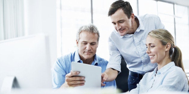 Three businesspeople looking at a digital tablet while working together in their office