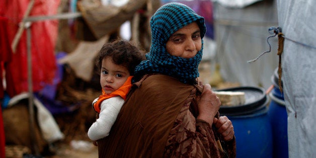 In this picture taken Monday, Jan. 4, 2016, a Syrian refugee woman carries her baby on her back as she walks in mud from the heavy rain, at a refugee camp in the town of Hosh Hareem, in the Bekaa valley, east Lebanon. A snowstorm engulfed Lebanon on the first day of the new year, cutting off mountain roads, isolating villages and worsening living conditions for tens of thousands of Syrian refugees. (AP Photo/Hassan Ammar)