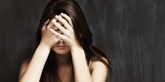 A studio shot of a sad young woman holding her head in her hands