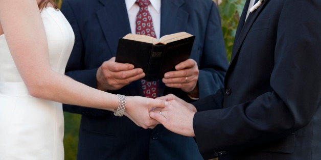 Bride and Groom holding hands at the altar as the minister oversees the reading of the vows. The wedding is taking place in N