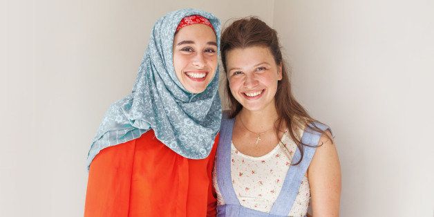 friendship of the religions concept: muslim and christian girl standing together and smiling at camera
