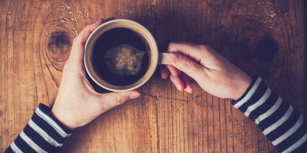 Lonely woman drinking coffee in the morning, top view of female hands holding cup of hot beverage on wooden desk, retro toned.