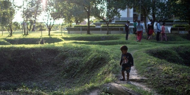 This photo taken on November 5, 2014 shows a child looking at the site of mass graves for victims of the Khmer Rouge at the Choeung Ek killing fields in Phnom Penh. Nearly a quarter of Cambodia's population was wiped out by starvation or execution during the Khmer Rouge's brutal rule over Cambodia that lasted from 1975 to 1979. AFP PHOTO/ ALEX OGLE (Photo credit should read Alex Ogle/AFP/Getty Images)