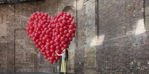 Woman in empty warehouse hugging red heart made of balloons