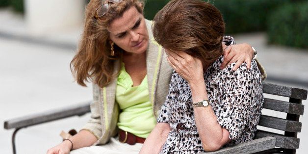 Senior woman with her hands on her head looking down sitting in a park bench with her daughter consoling her
