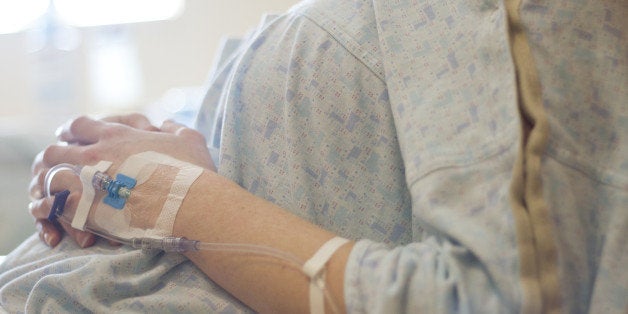 A pregnant woman in the early stages of labor rests in a hospital bed with her arms on her stomach. An IV is seen in her left hand.