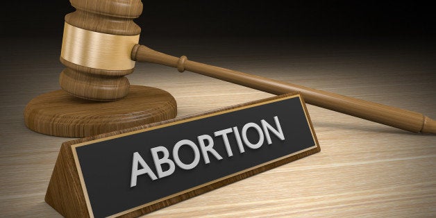 A wooden court gavel next to a sign that says abortion on it.