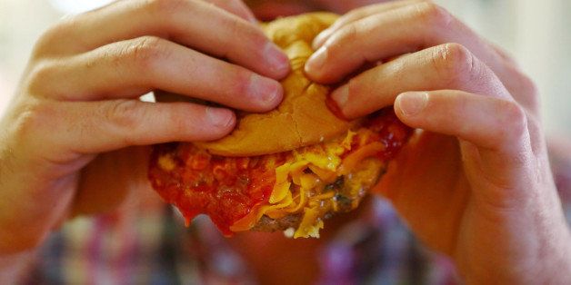 A man eats a messy hamburger dripping with cheese and sauce.