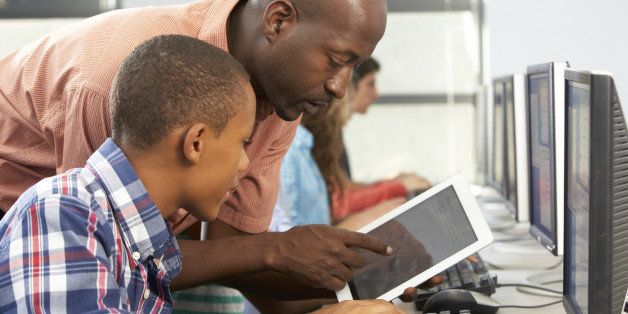 Teacher Helping Boy To Use Digital Tablet In Computer Class Having A Discussion