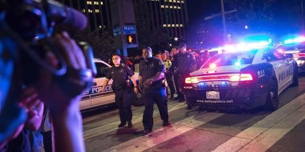 TOPSHOT - Bystanders stand near pollice baracades following the sniper shooting in Dallas on July 7, 2016. A fourth police officer was killed and two suspected snipers were in custody after a protest late Thursday against police brutality in Dallas, authorities said. One suspect had turned himself in and another who was in a shootout with SWAT officers was also in custody, the Dallas Police Department tweeted. / AFP / Laura Buckman (Photo credit should read LAURA BUCKMAN/AFP/Getty Images)