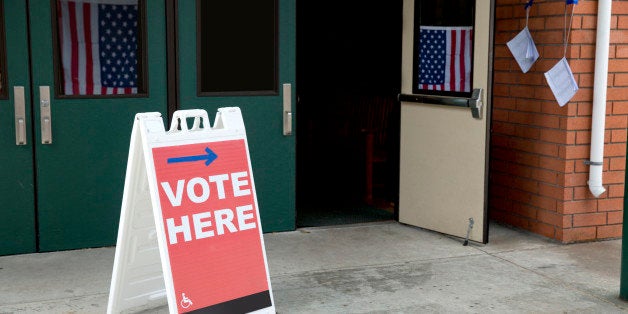 Stock photo of a vote here sign at an American voting location with American flags in the background