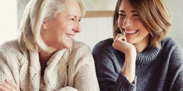 Laughing mother and daughter in sweaters drinking coffee