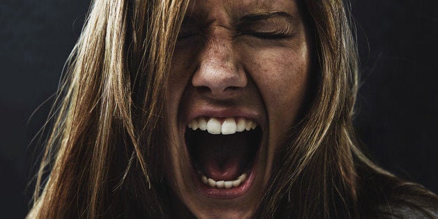 A young woman screaming uncontrollably while isolated on a black background