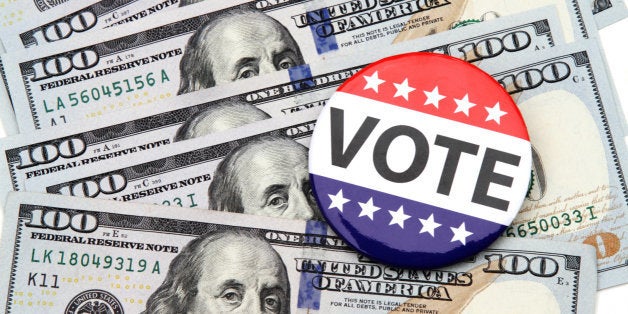 VOTE campaign button on top of scattered hundred dollar bills spread out beneath it. Concept image illustrating election funding, political donations, Super Pac money, political bribes.