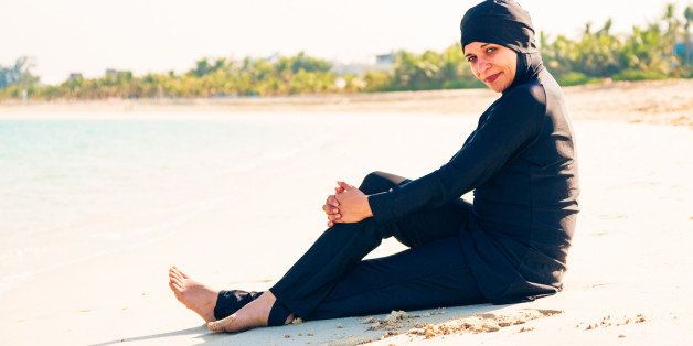 young woman wearing burkini sitting by the beach in dubai